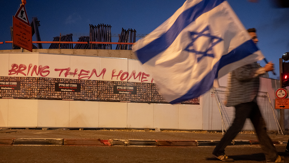 JERUSALEM - NOVEMBER 18: A person carrying an Israeli flag walks by graffiti that reads, "Bring them home now" on November 18, 2023 in Jerusalem, Unspecified. Families and supporters of the hostages taken by Hamas in its Oct 7 attack commenced a multiday march from Tel Aviv to Jerusalem, where they will demonstrate in front of the Prime Minister's office. According to Israeli officials, over 240 hostages are being held by Hamas in the Gaza Strip. (Photo by Alexi J. Rosenfeld/Getty Images)
